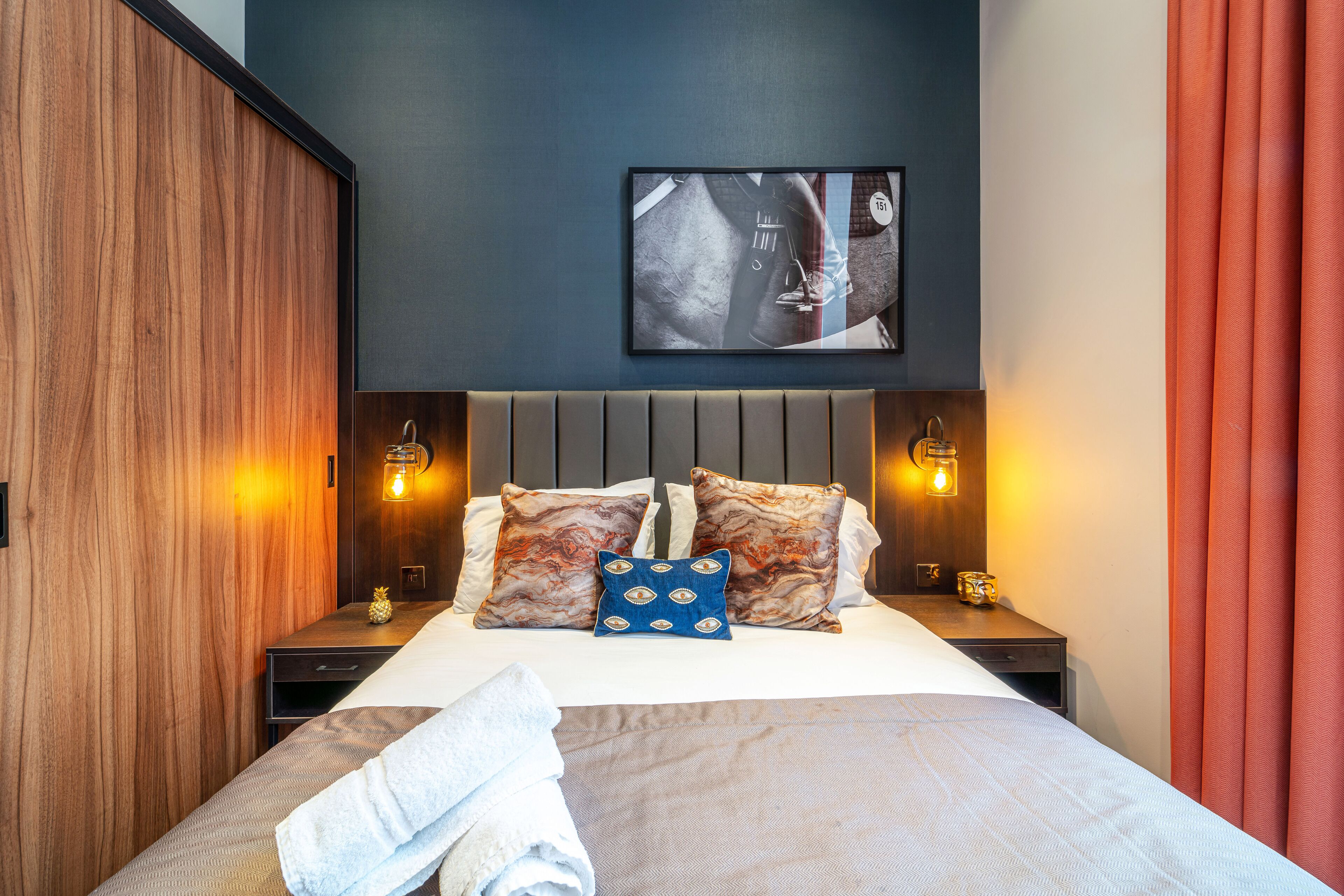 A neatly made bed with a blue and white patterned pillow, a wooden headboard, and a wall-mounted picture.