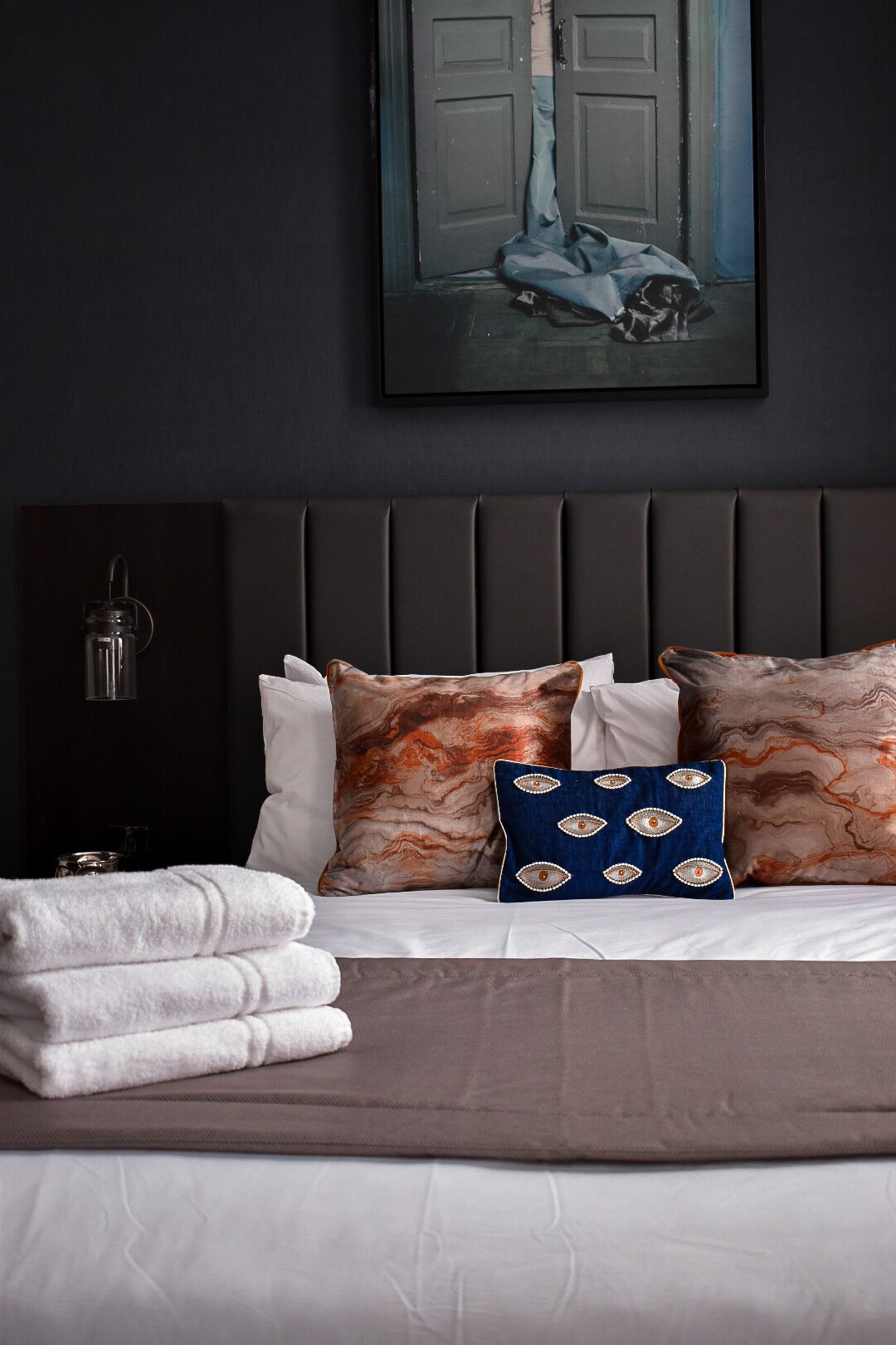 A neatly made bed with a dark headboard, white and patterned pillows, and folded towels.