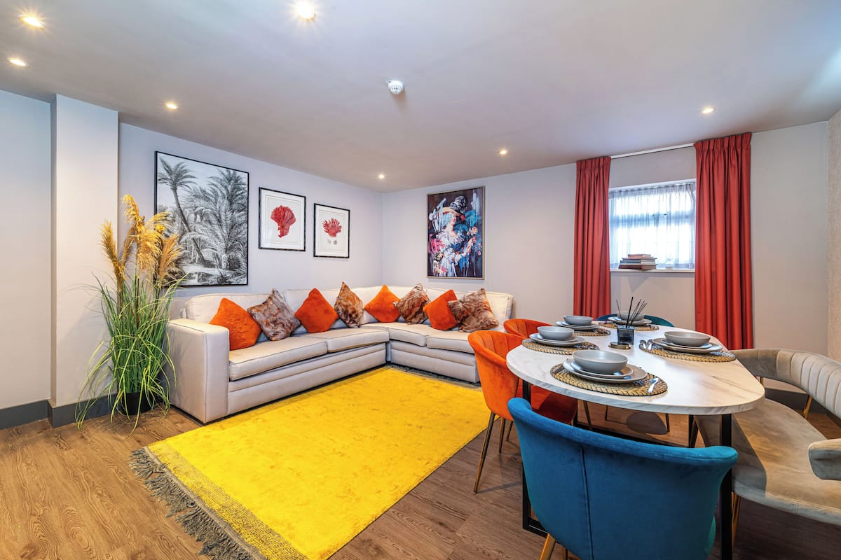 A modern living room with a sectional sofa, a dining table with chairs, and a yellow rug.