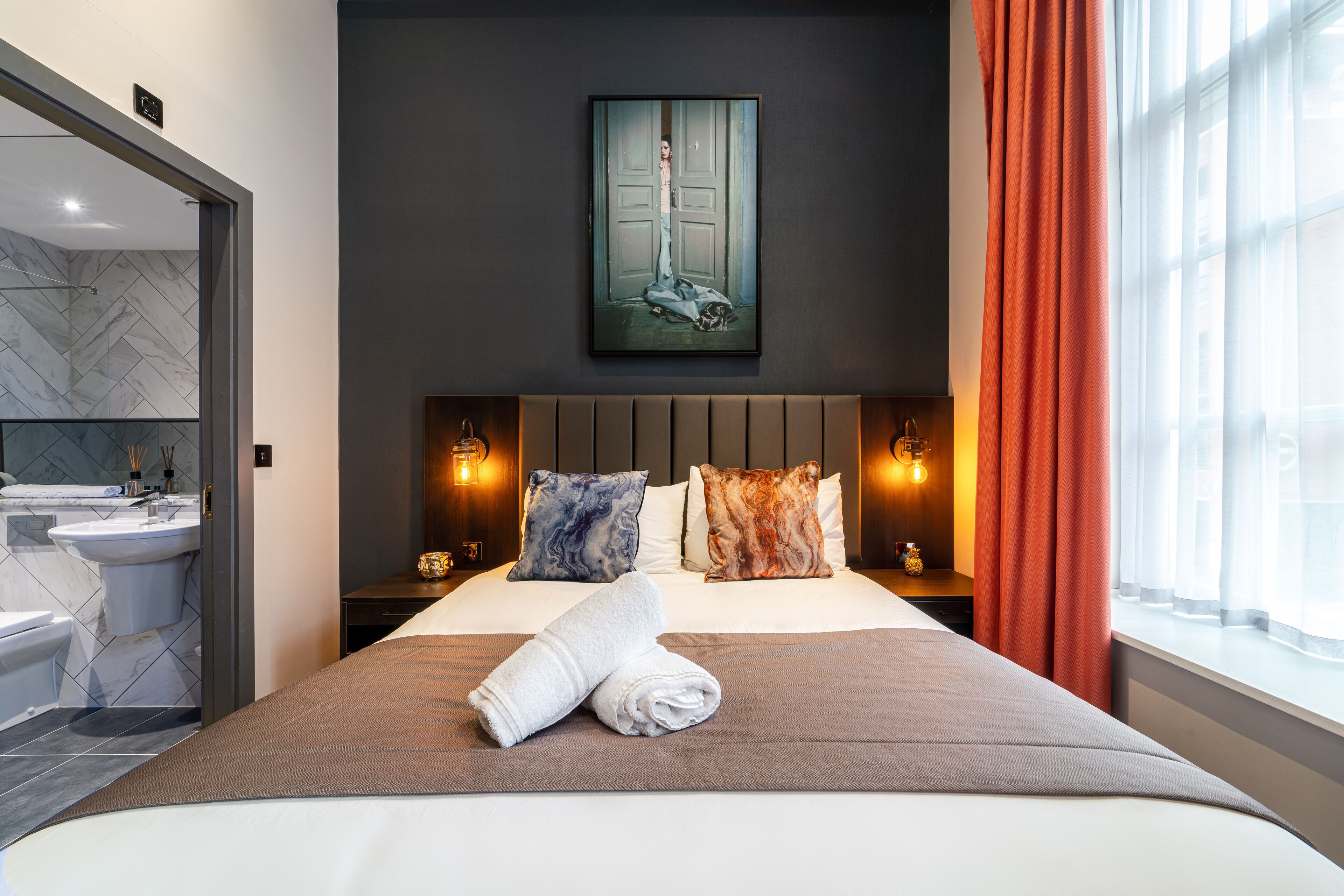 Una habitación de hotel moderna con una cama grande, un baño con detalles de mármol y un cuadro sobre la cama.