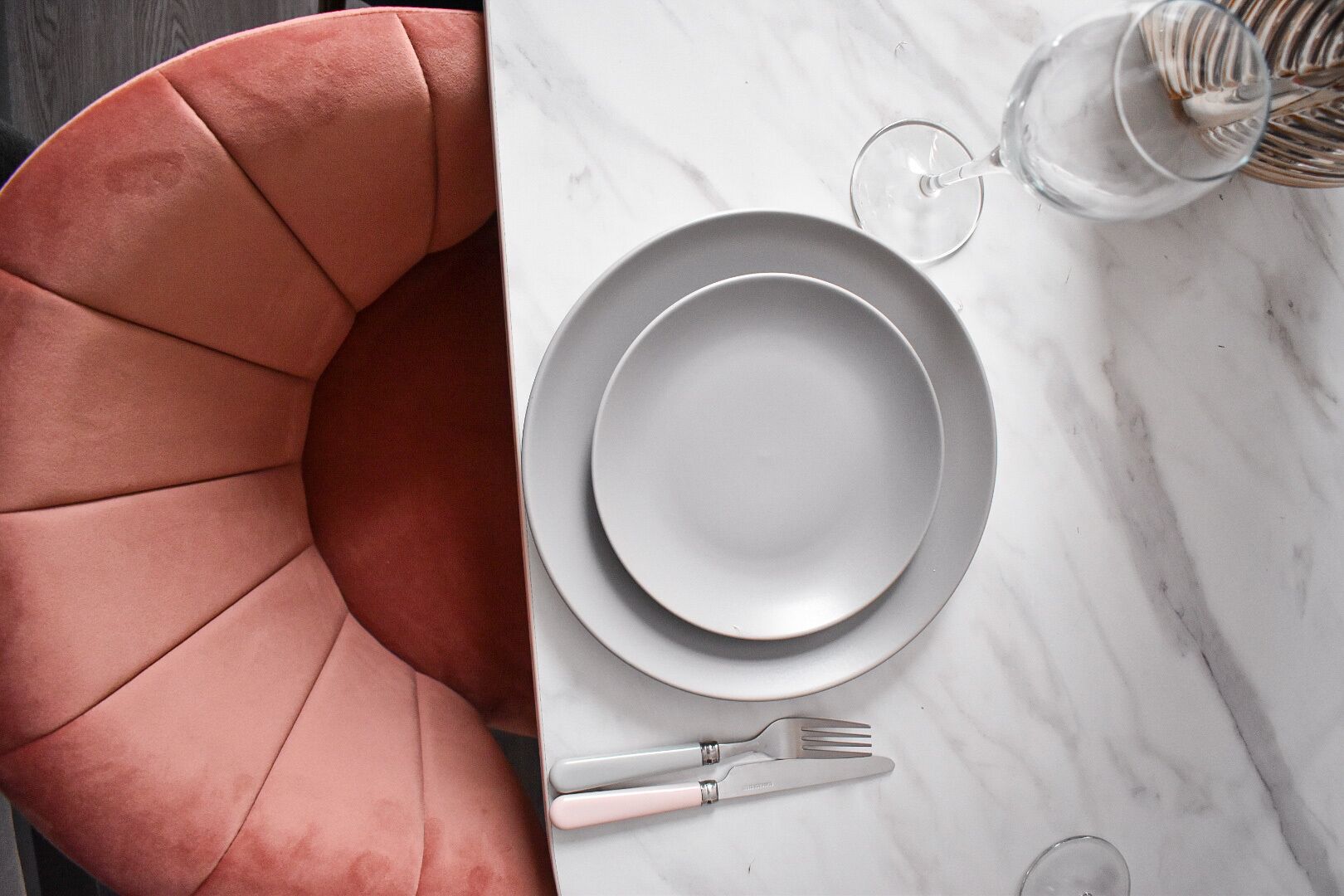 Une table à manger avec un plateau en marbre blanc, une paire de couverts et un verre d’eau.