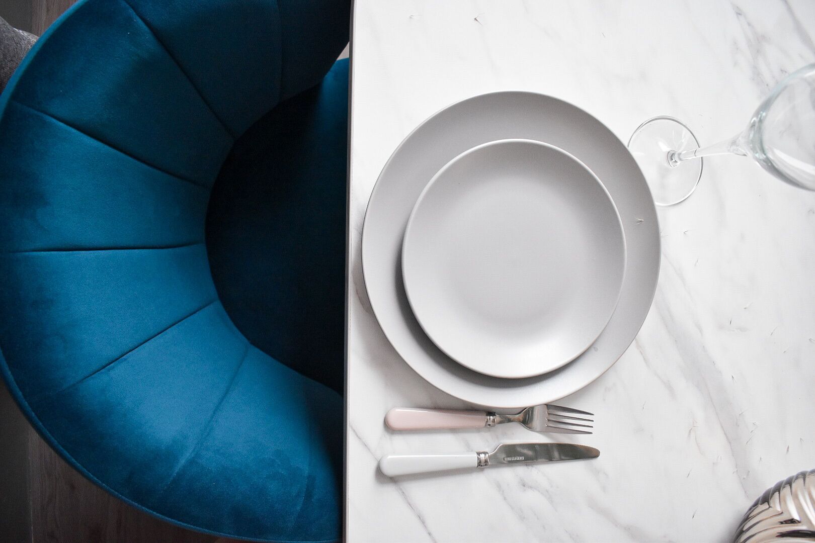 A dining setup with a white marble table, a blue chair, and a wine glass.
