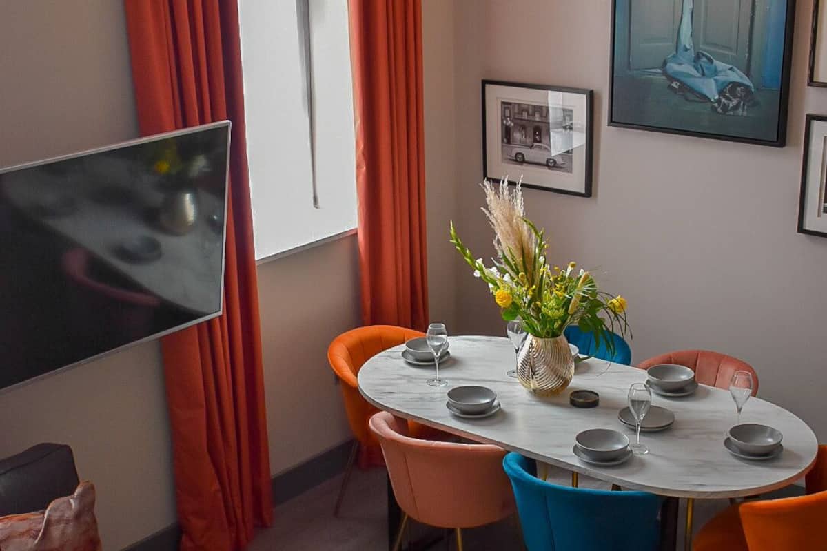 A modern dining area with a round table, orange chairs, and a vase of flowers.