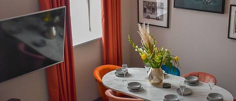 A modern dining area with a round table, orange chairs, and a vase of flowers.