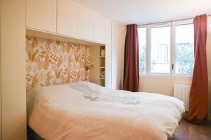 A bedroom with a bed, built-in wardrobe, and a window with curtains.