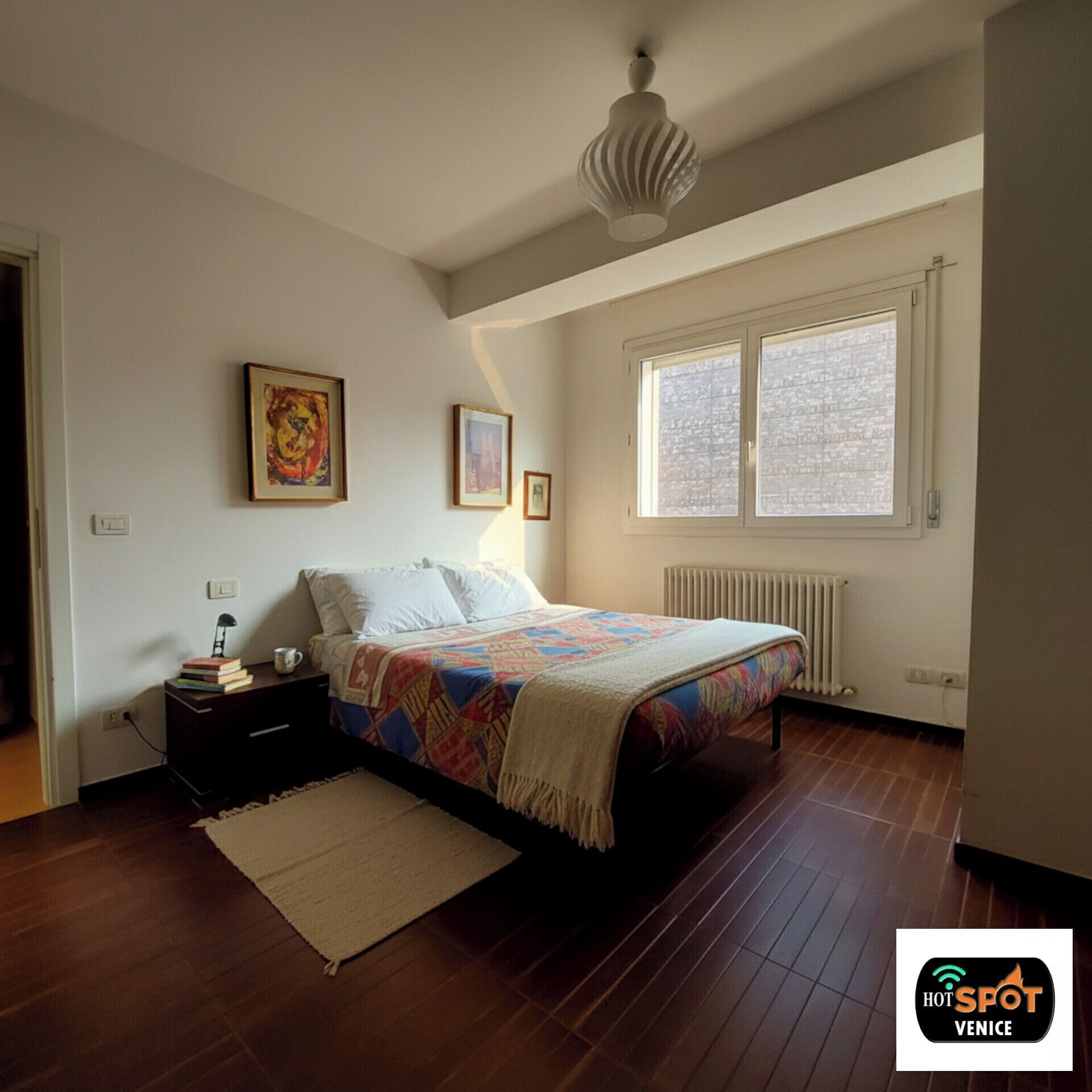 Ein Schlafzimmer mit einem Bett, einem Nachttisch, einer Lampe und einem Fenster.