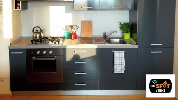 A modern kitchen with stainless steel appliances, a gas stove, and a built-in oven. There are cabinets with handles and a countertop with a cutting board and a potted plant. - Hotspot Venice Ca Marcello 2000 Palace (Venezia)