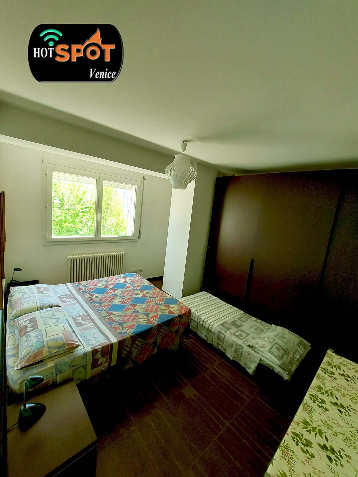 A small, well-lit room with a bed, a desk, and a window.