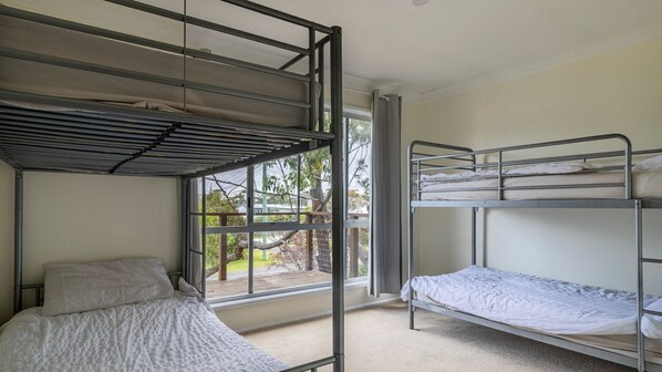 A dormitory room with bunk beds, a window with a view of trees, and a door. - Bush 2 Beach in Berrara (Berrara)