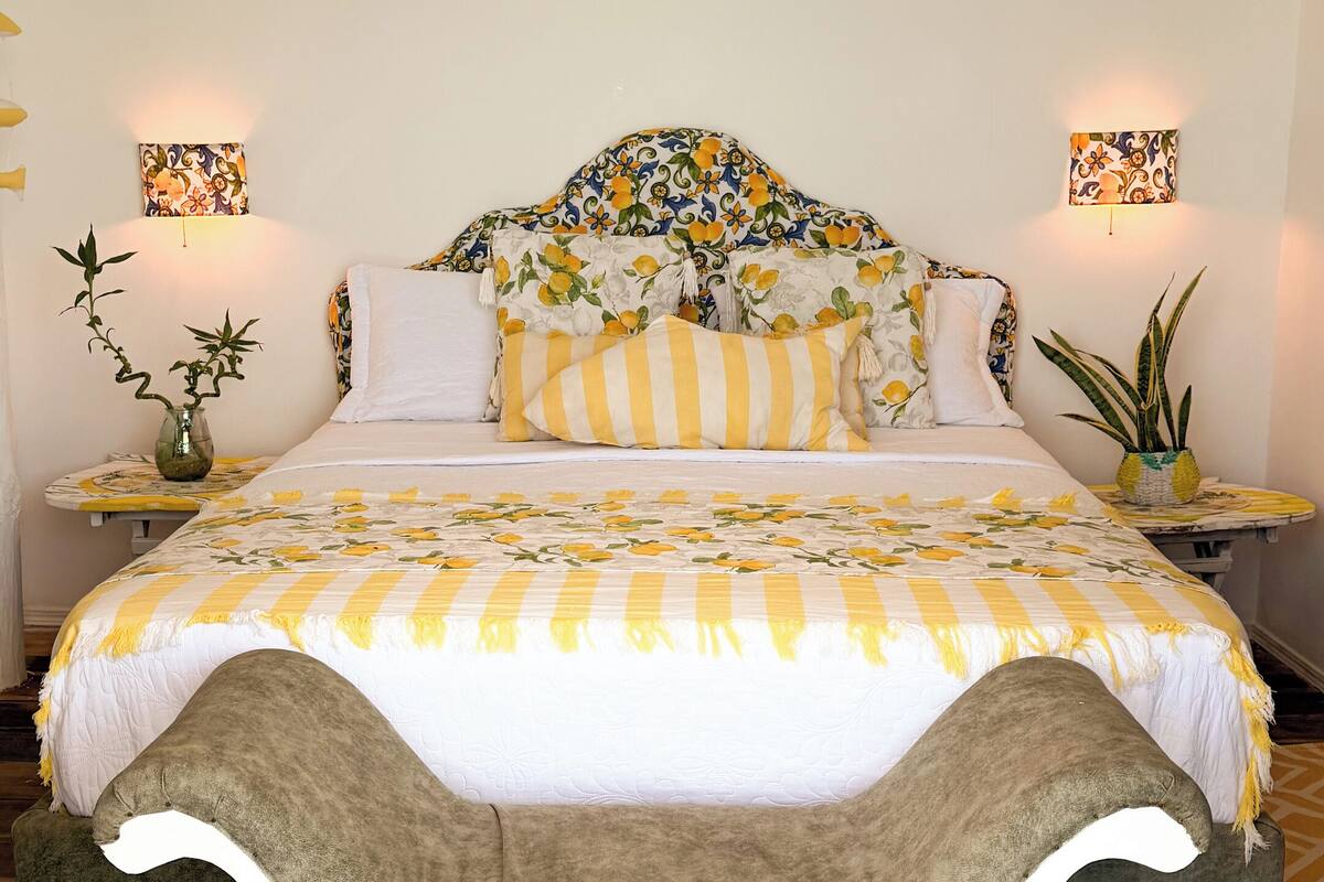 A bedroom with a bed, bedside tables, a chandelier, and a welcome mat.