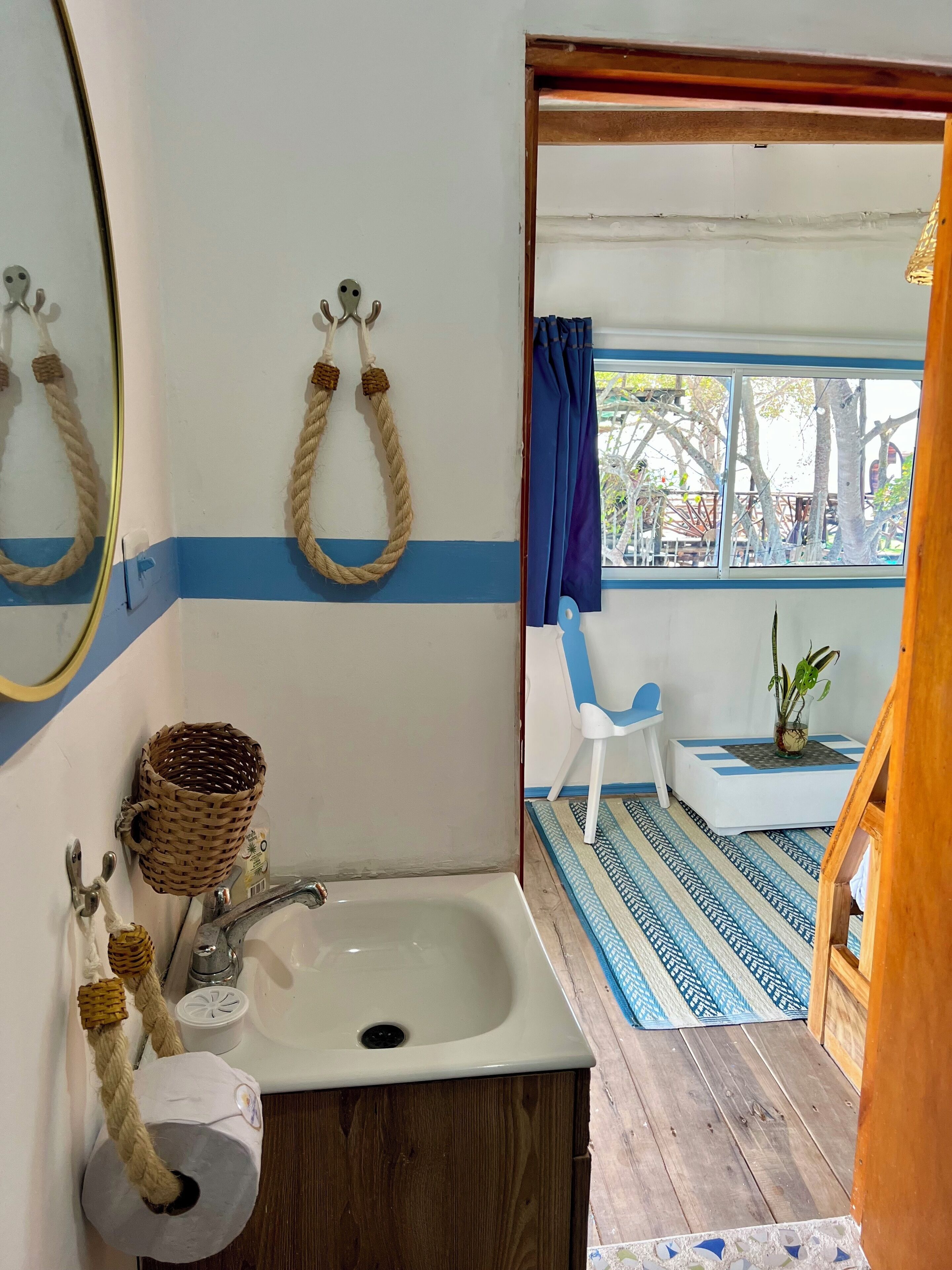 A bathroom with a sink, mirror, and towel rack. There is a window with blue curtains and a view of trees outside.