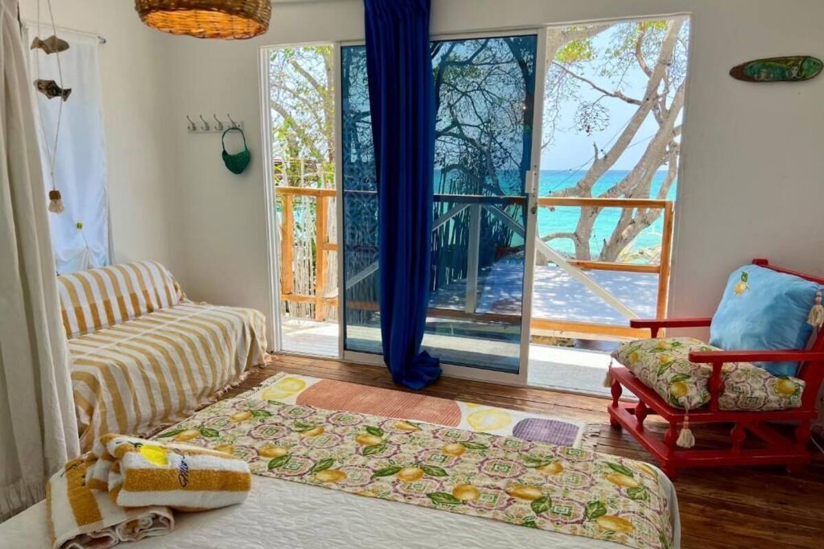 A bedroom with a bed, a chair, a view of the beach, and a balcony.