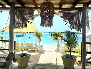 A beachside seating area with a view of the ocean, featuring a wooden deck, potted plants, and a thatched roof structure. - Mio Mio Beach (Cartagena)