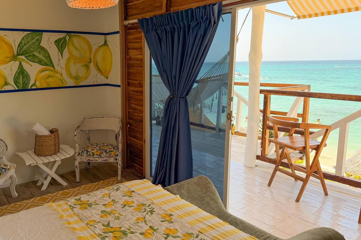 A room with a bed, two chairs, a small table, and a view of the sea.