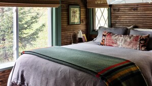 Ein gemütliches Schlafzimmer mit einem großen Bett, einem Fenster mit Blick auf Bäume und einer Holzbalkendecke.
