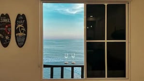 Una habitación con un amplio ventanal con vistas al mar, dos adornos de temática surf y dos copas de vino sobre el alféizar.