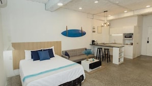 Una habitación de hotel moderna con una cama, un sofá, una pequeña cocina y una mesa de comedor.