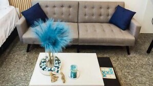 Una sala de estar con un sofá color beige, una mesa de centro blanca y una tabla de surf azul en la pared.