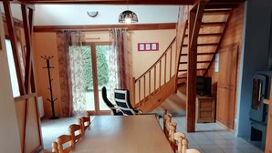 Un comedor amplio con una larga mesa de madera y sillas, un perchero y una escalera que lleva a un nivel superior.