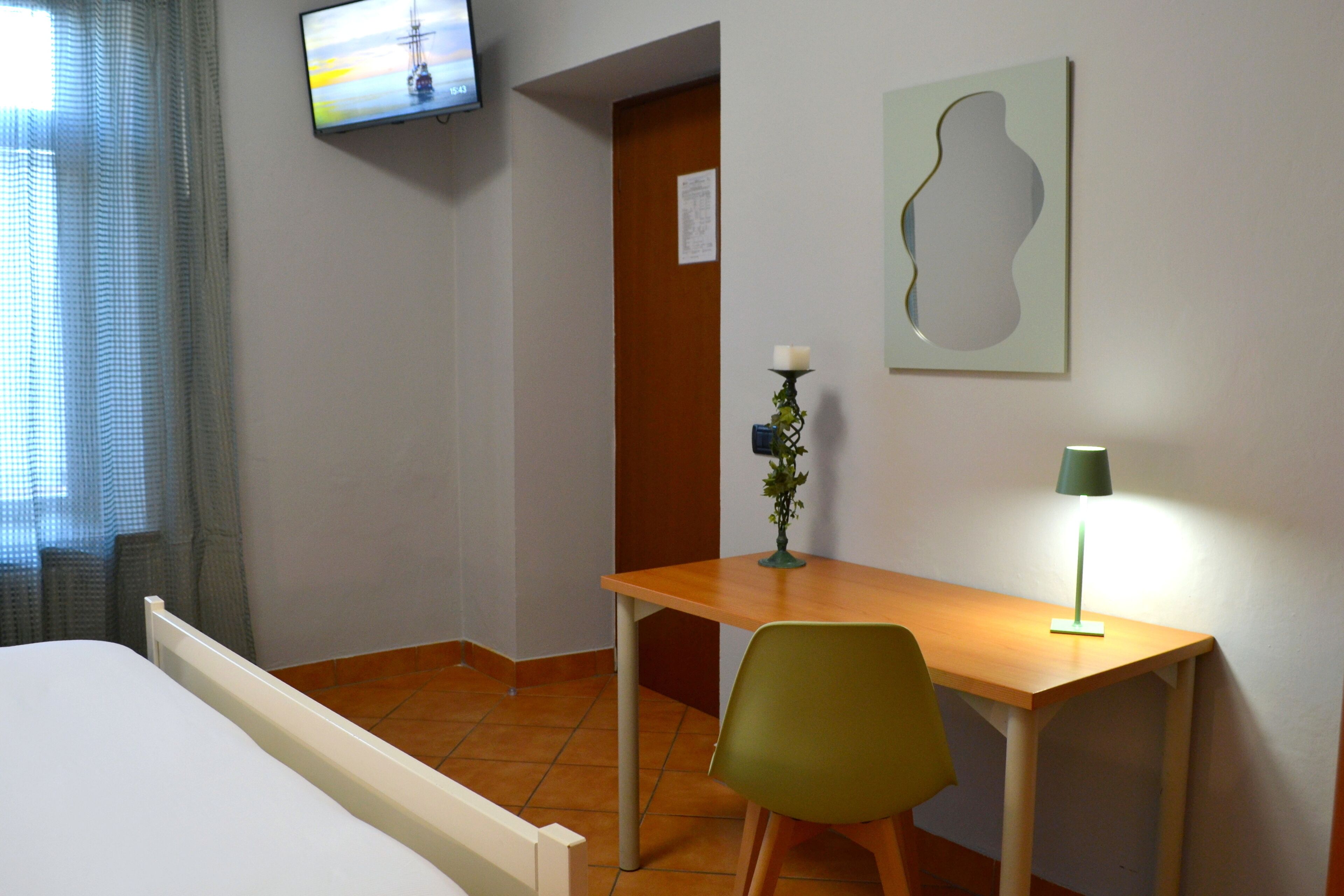 A hotel room with a bed, a desk, a chair, a TV, a lamp, and a wall art piece.