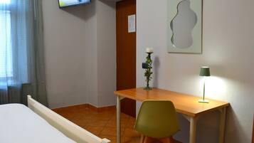 Ein Hotelzimmer mit einem Bett, einem Schreibtisch, einem Sessel, einem Fernseher, einer Lampe und einem Wandbild.