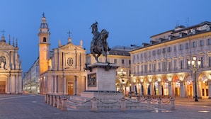 Une place historique, dominée par une église imposante, une statue et des bâtiments aux façades illuminées.