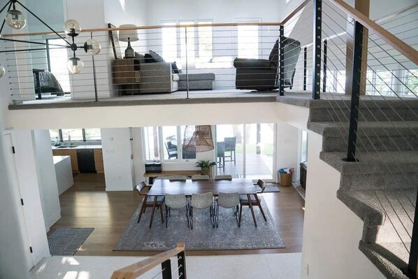 A spacious loft with a dining area, kitchen, and a staircase leading to a lofted seating area. - The Highland Loop Experience on Ottertail Lake (Battle Lake)