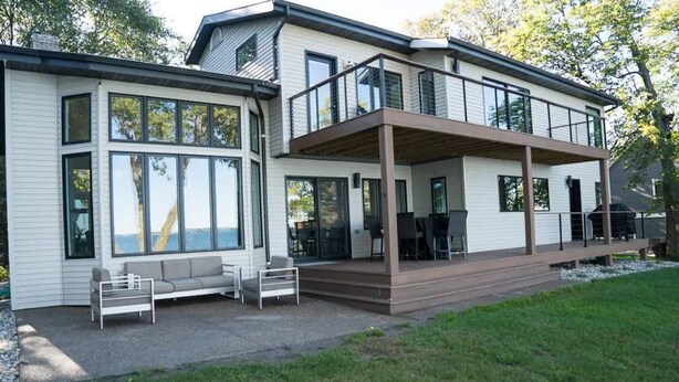 A modern two-story house with a covered patio, large windows, and outdoor seating. - The Highland Loop Experience on Ottertail Lake (Battle Lake)