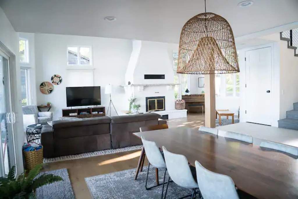 Un vaste espace de vie comprenant une grande table à manger en bois, un canapé confortable, un téléviseur à écran plat et un luminaire suspendu en osier.