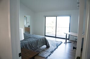 A bedroom with a bed, a desk, a chair, and a large window.