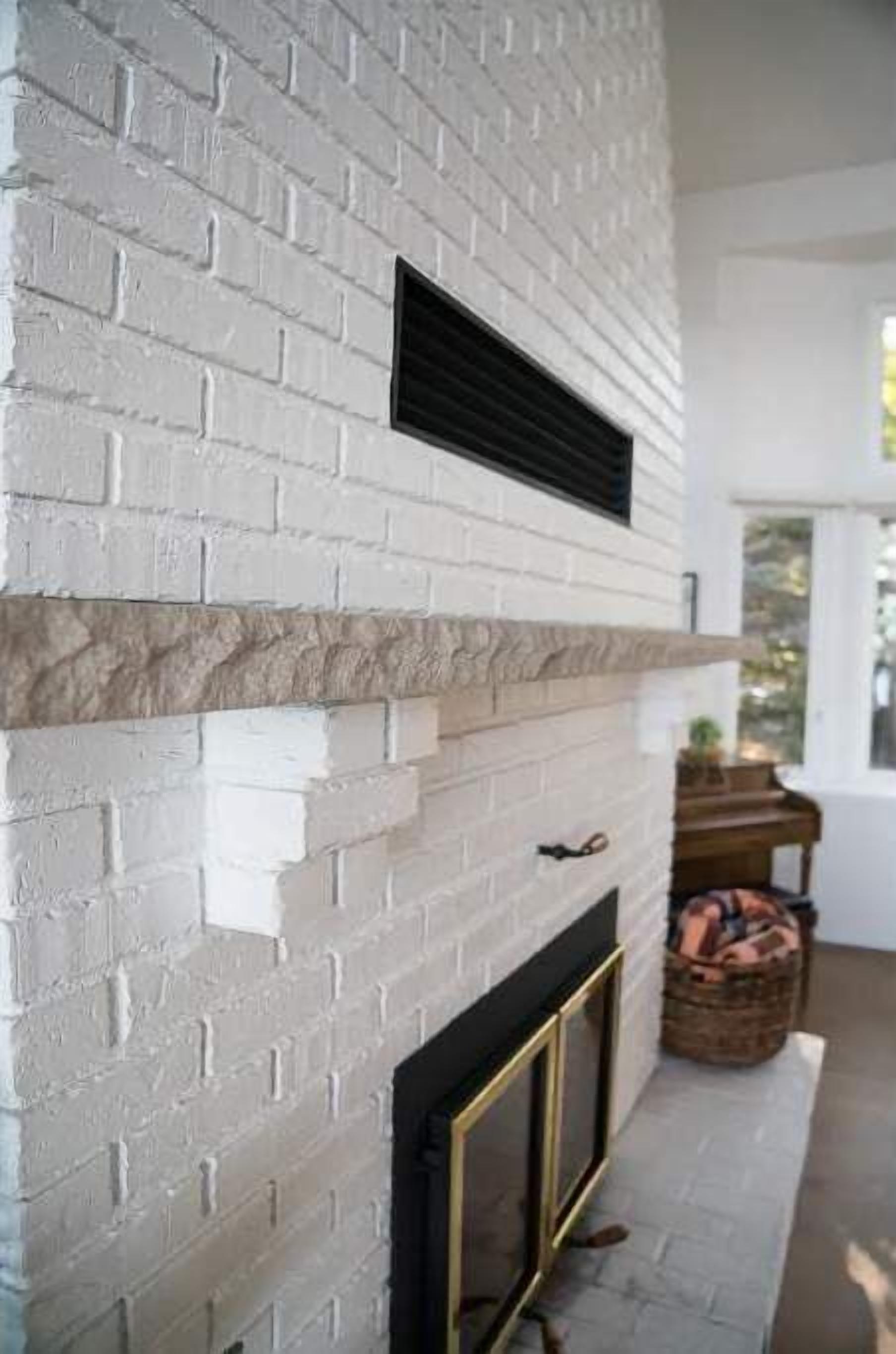A white brick fireplace with a black vent, a gold-framed glass door, and a stone mantle.