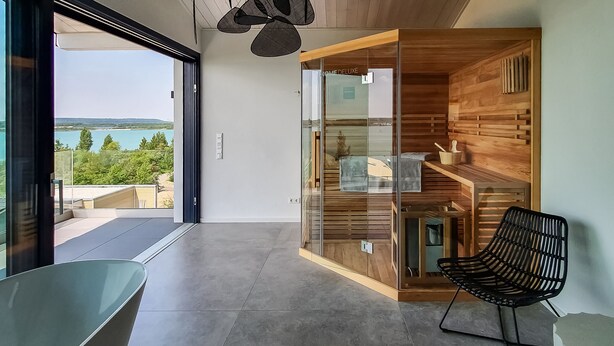 Una habitación moderna con una puerta de cristal que da a un balcón con vistas a un cuerpo de agua.