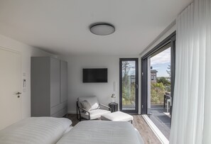 Een moderne slaapkamer met twee bedden, een zithoek, een televisie en een balkon met uitzicht.