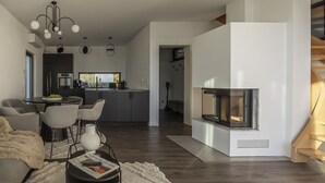 Una sala de estar moderna con chimenea, un comedor con una mesa redonda y sillas, y una cocina al fondo.