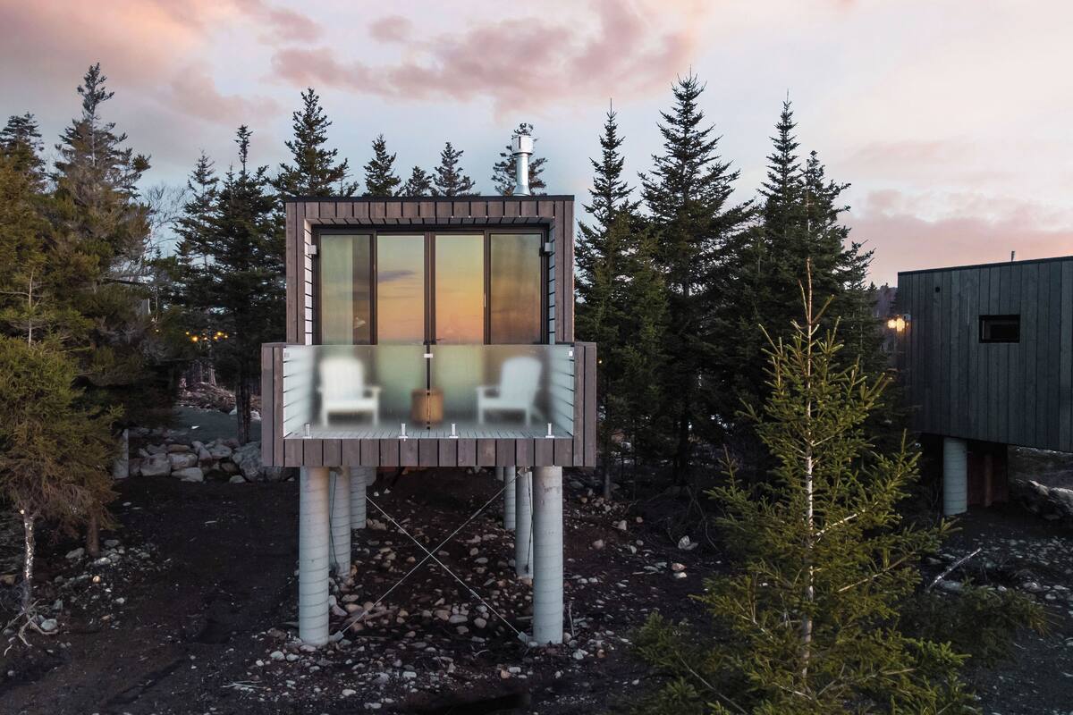 Una moderna casa sull'albero con un balcone in vetro, immersa in una fitta foresta.