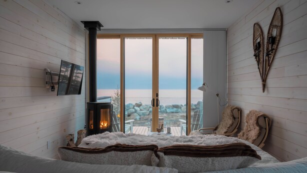 A cozy bedroom with a large window overlooking a rocky landscape, a fireplace, and a bed with fluffy bedding. - White Point Beach Resort (Hunts Point)