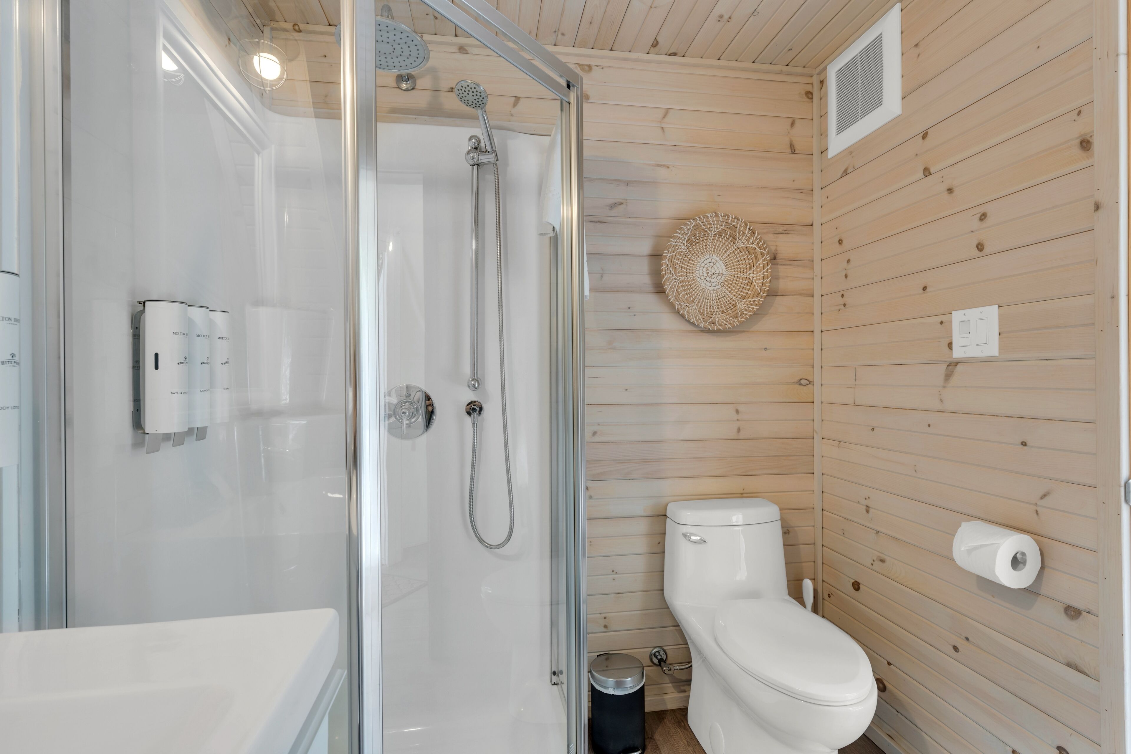 Ein Badezimmer mit einer gläsernen Dusche, einer weißen Toilette und einer Holzwand.