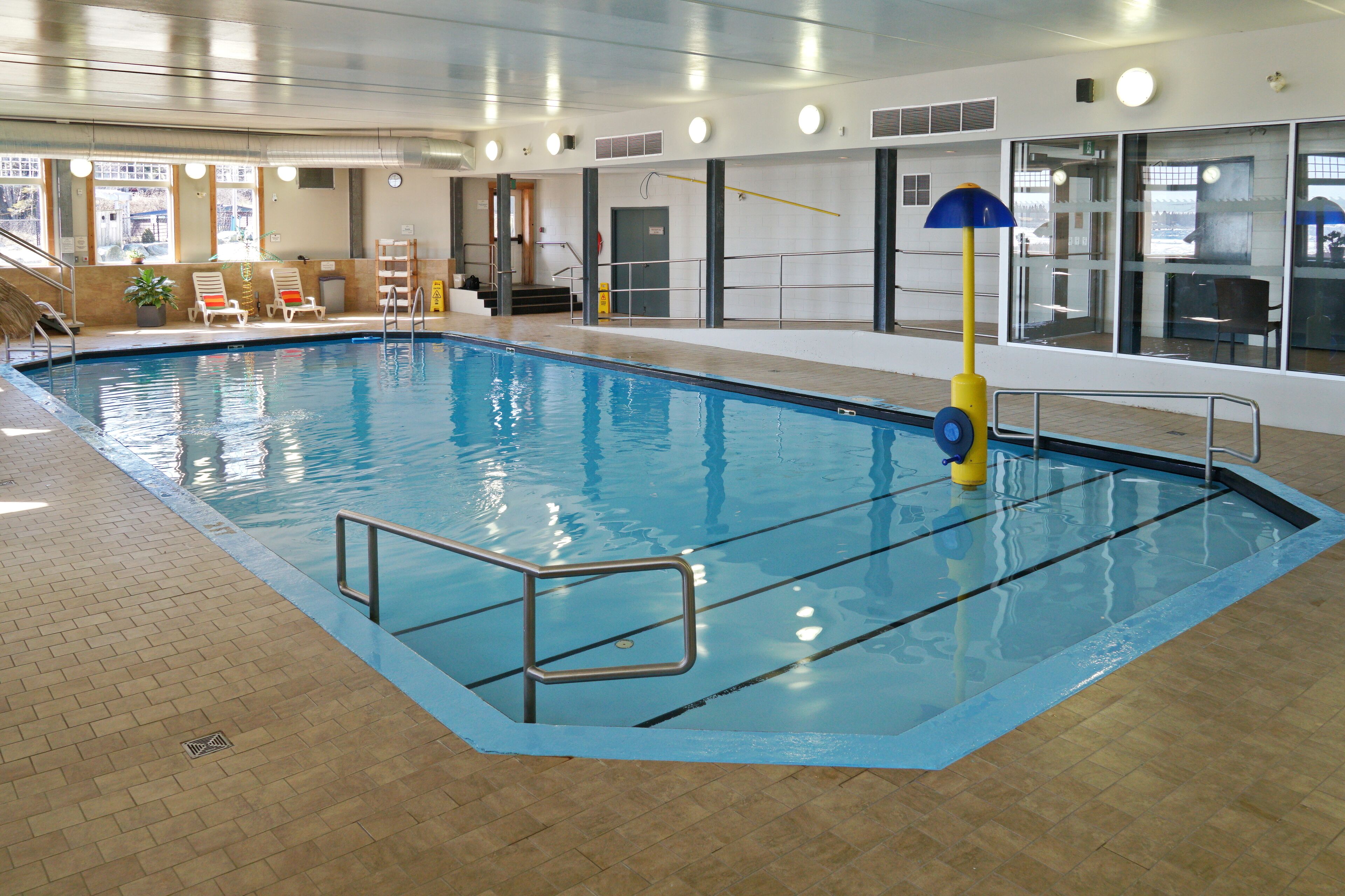 An indoor swimming pool with clear water, a lifeguard stand, and lounge chairs.