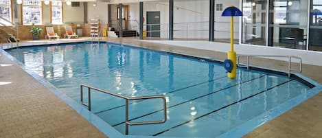An indoor swimming pool with clear water, a lifeguard stand, and lounge chairs.