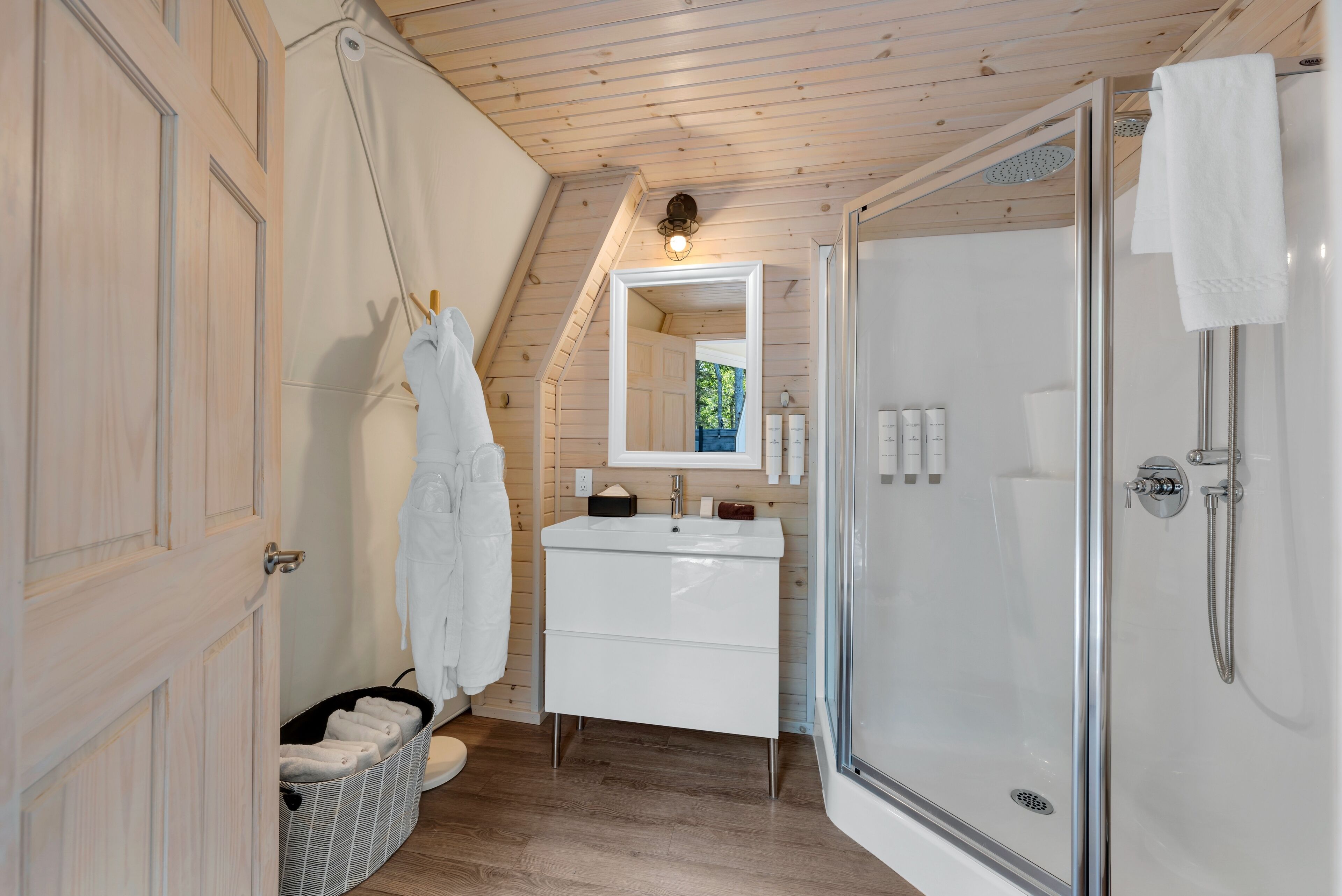 A modern bathroom with a wooden ceiling, a glass shower enclosure, a white sink with a mirror, and a towel rack.