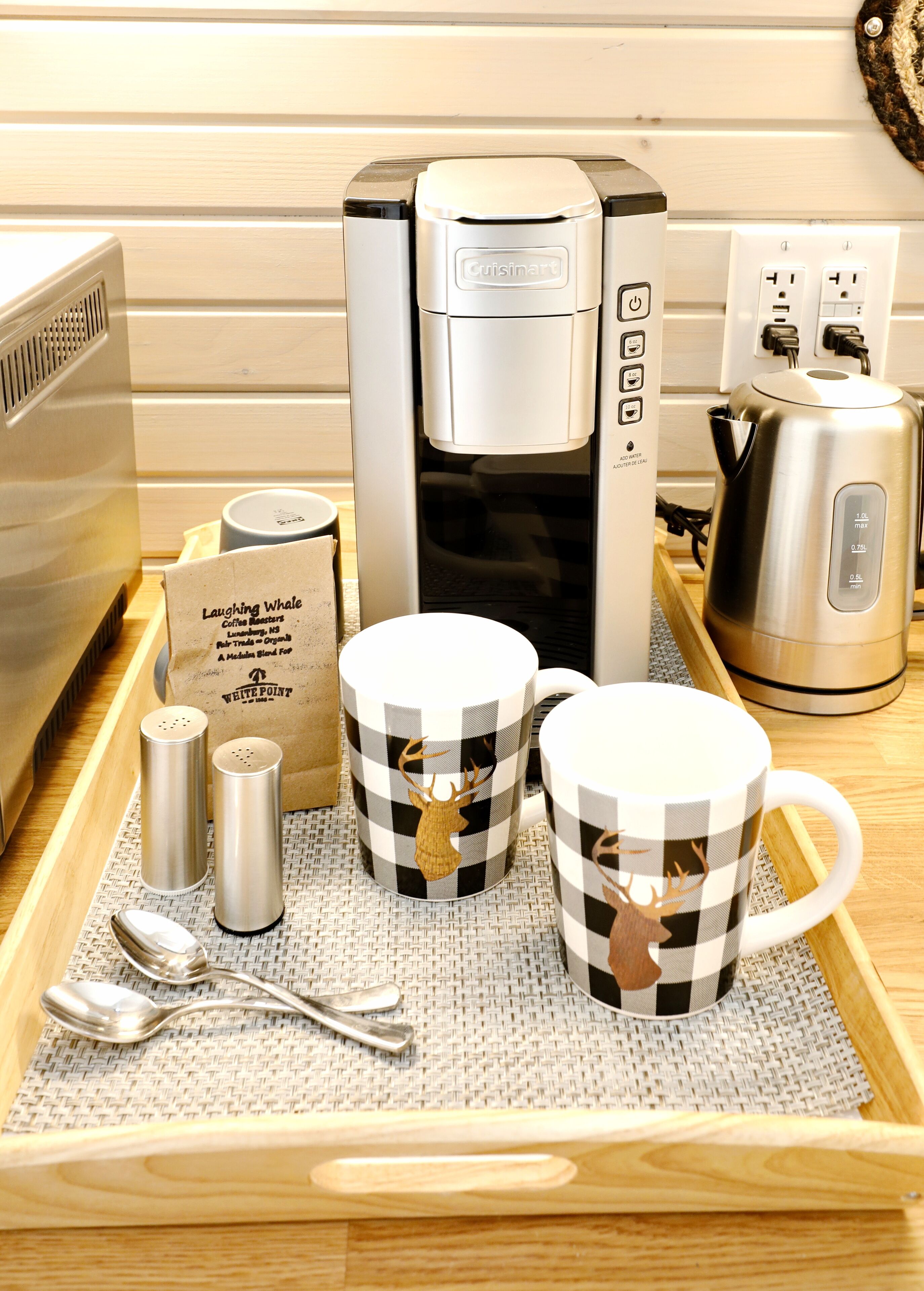 A coffee maker, two mugs with a checkered pattern, salt and pepper shakers, and a spoon on a tray.