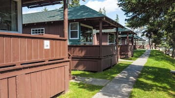 A row of wooden cabins with a number sign '28' on the side, a covered porch, and a concrete pathway between them.