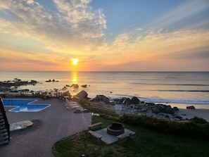 Sonnenuntergangsblick von einer Strandterrasse mit Pool, Liegestühlen und Feuerstelle.