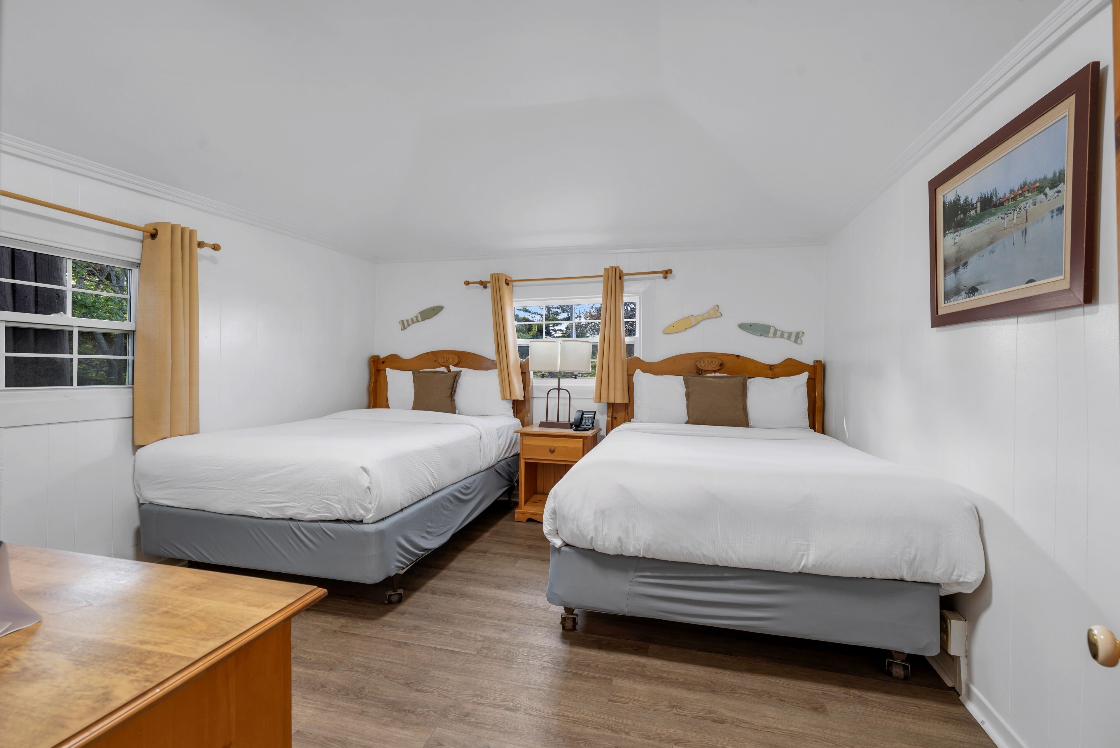 Una habitación con dos camas individuales, mesitas de noche de madera, una pequeña mesa y un ventanal con cortinas.