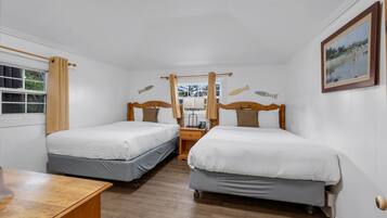 Una habitación con dos camas individuales, mesitas de noche de madera, una pequeña mesa y un ventanal con cortinas.