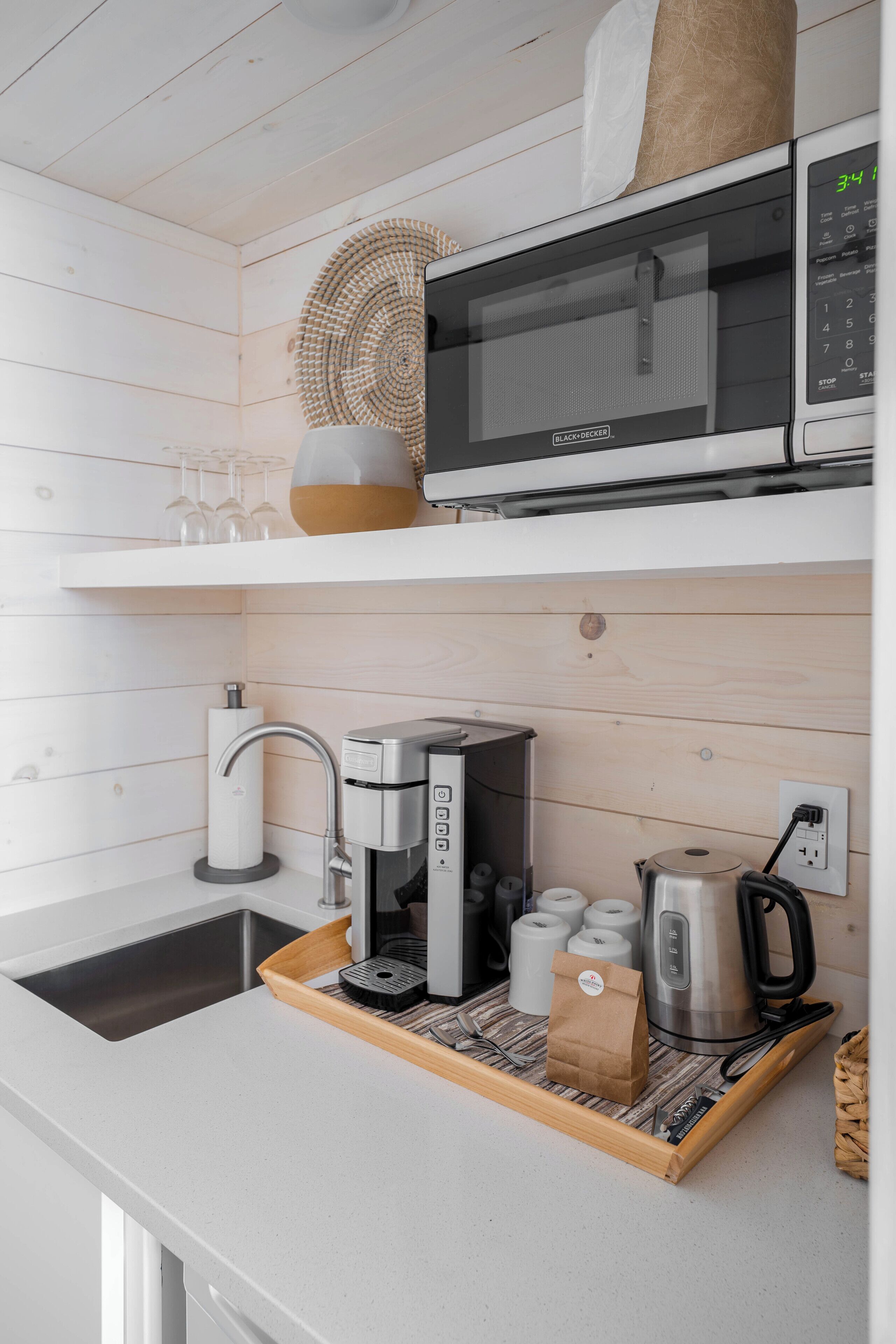 A kitchen with a microwave, coffee maker, and kettle on a wooden tray.