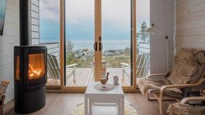 A cozy living room with a wood-burning stove, a comfortable chair, and a view of the outdoors. - White Point Beach Resort (Hunts Point)