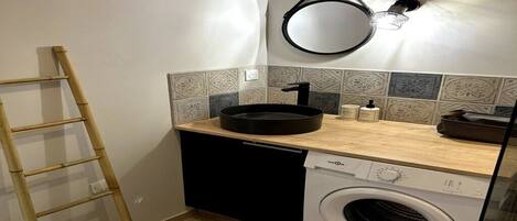 Een kleine keuken met een wasmachine, een spoelbak en een spiegel.