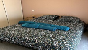 A neatly made bed with a floral-patterned bedspread and matching pillows, a blue towel, and a small bedside table with a lamp. - Le Cosy de Pauline et Flo (Cessenon-sur-Orb)