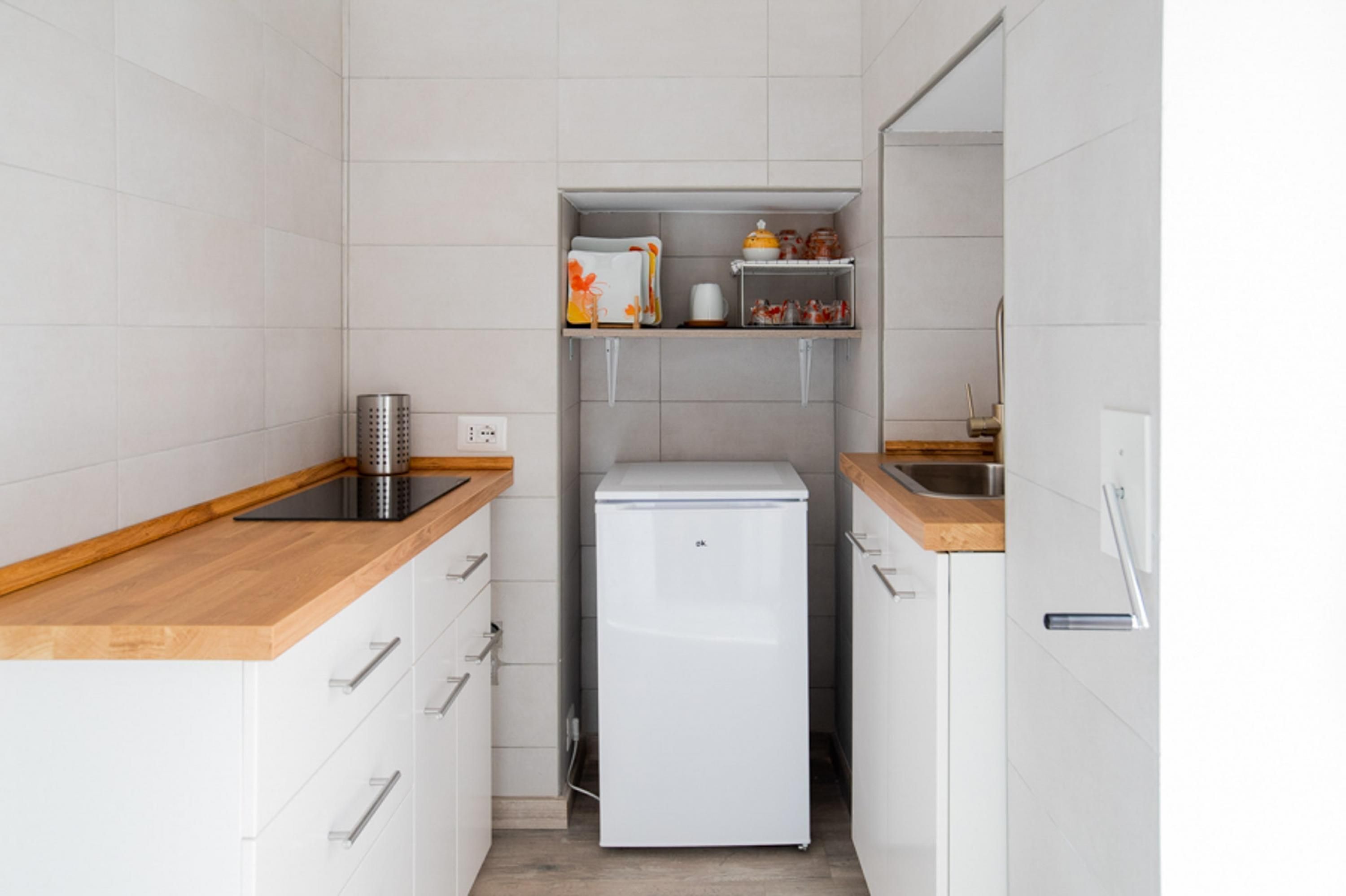 A compact kitchen with white cabinets, a wooden countertop, a white refrigerator, and a shelf with kitchen items.